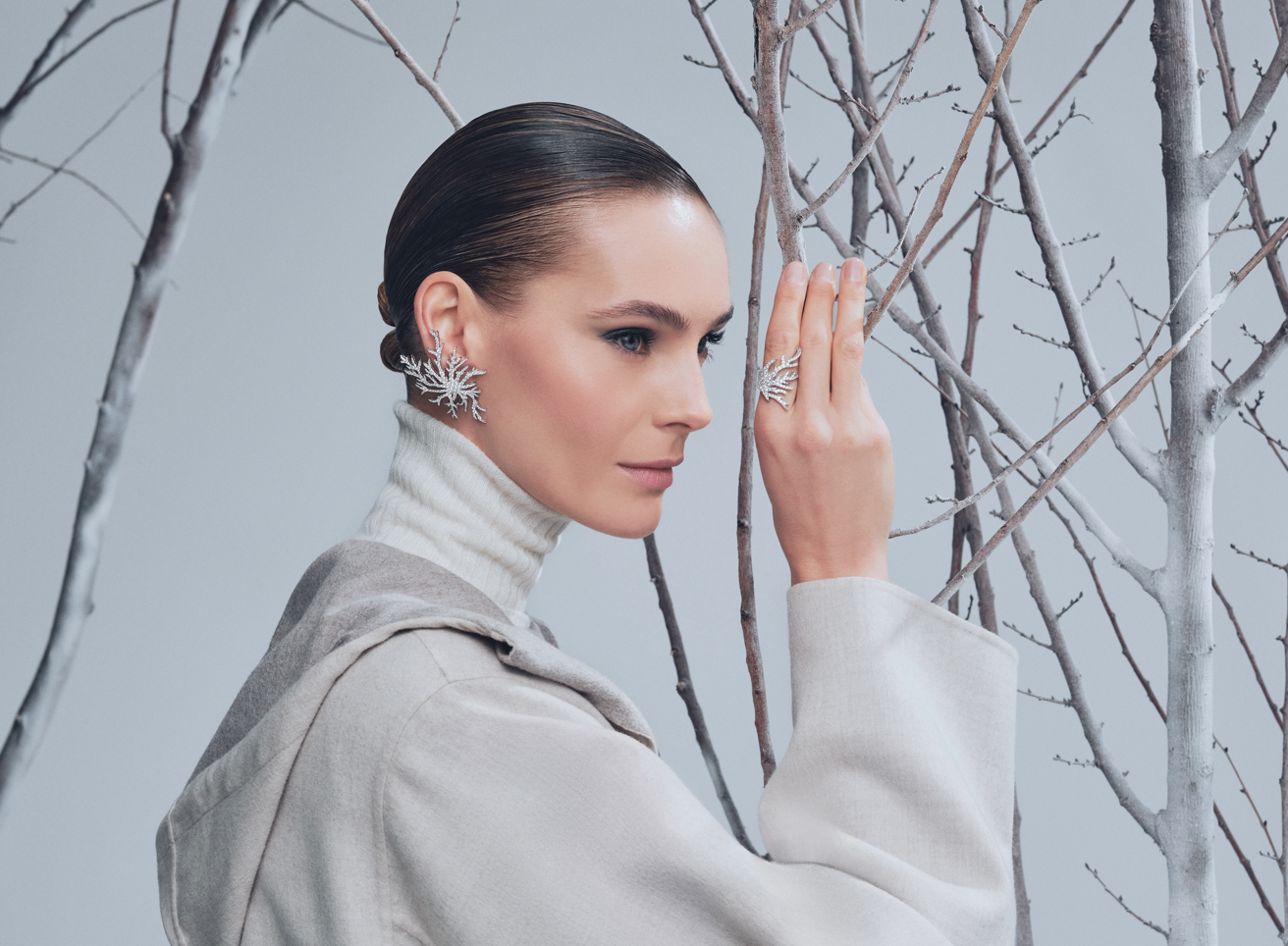 Modella di profilo con orecchino e anello a fiocco di neve in diamanti Antoine Incanto del Gelo, tra rami di betulla in un'ambientazione invernale